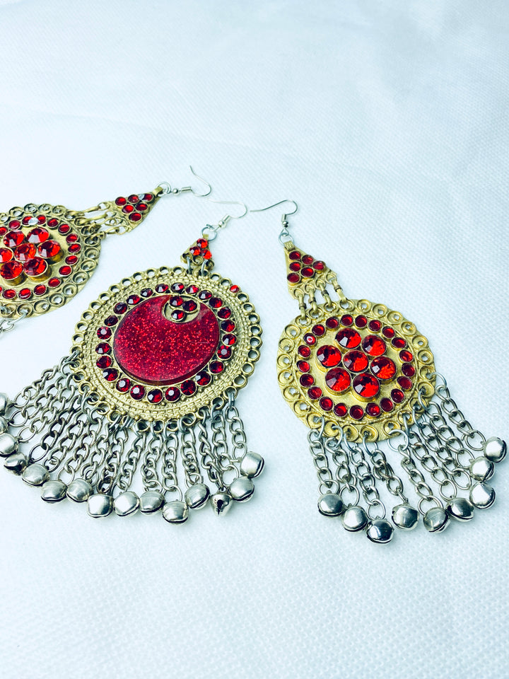 Ornate earrings with red gemstones and silver fringes on a white background