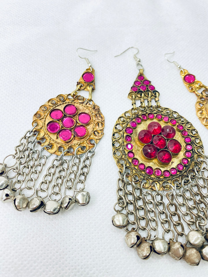 Pair of ornate earrings with pink gemstones and chain details on a white background