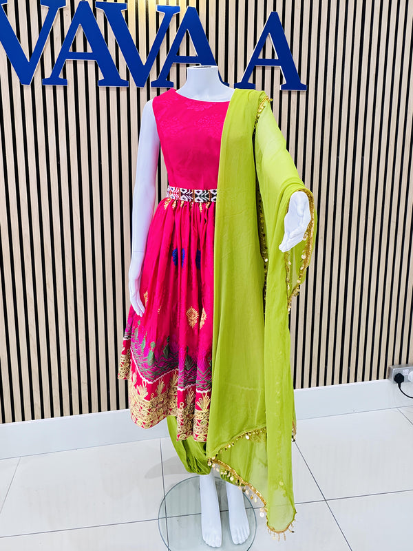 Mannequin wearing a pink afghan kuchi dress with a green dupatta against a striped wall with 'VAVA' branding.