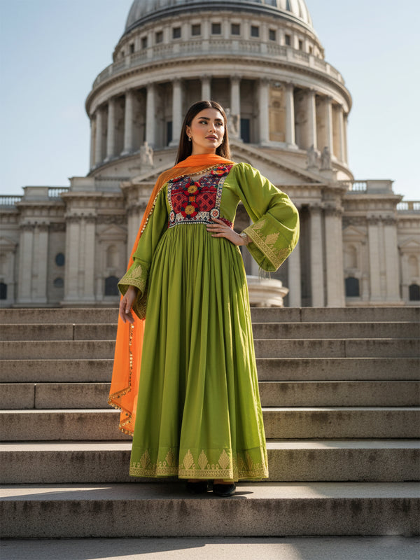 Woman in a green dress with orange dupatta standing on steps in front of a large building.