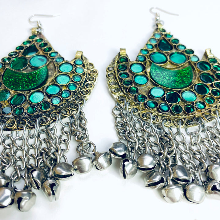 Ornate earrings with green gemstones and silver chains on a white background